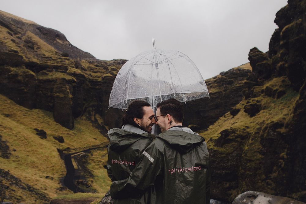 A couple shares a moment under a clear umbrella against dramatic mountain cliffs in the rain.