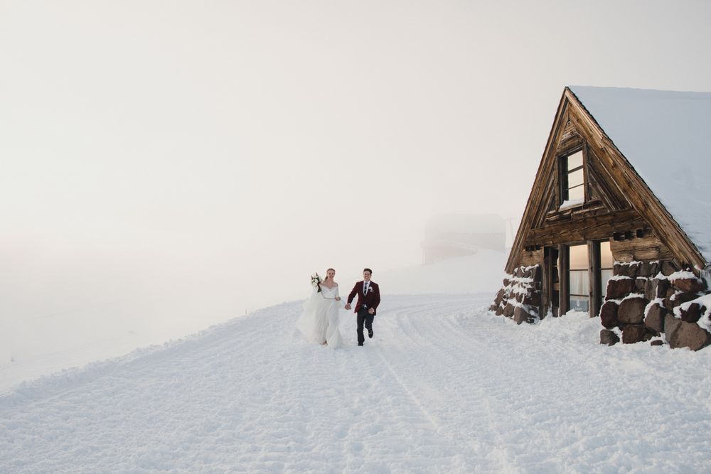 A distant view of a snowy A-frame cabin with two figures walking up a snow-covered hill.