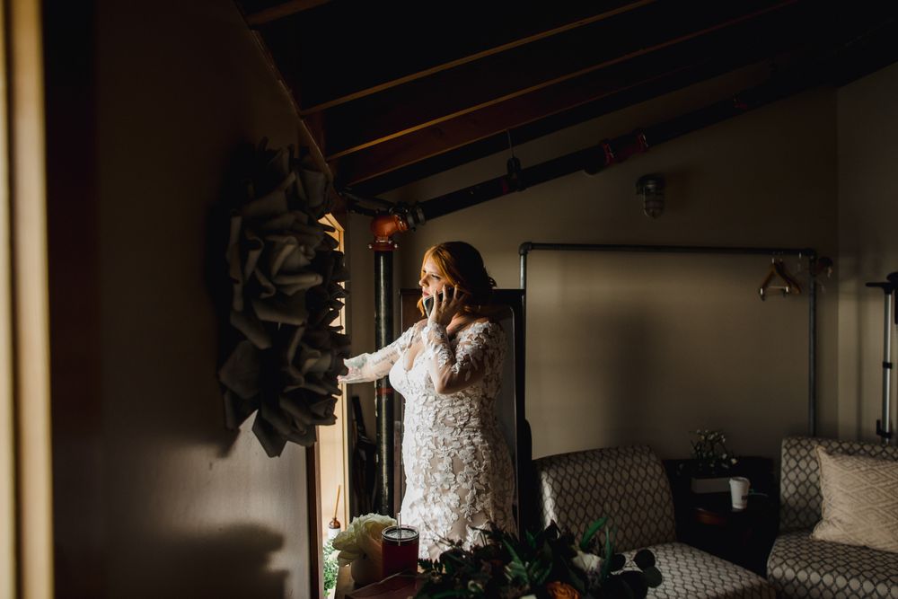 A white lace dress hangs in a dimly lit rustic room with decorative greenery.