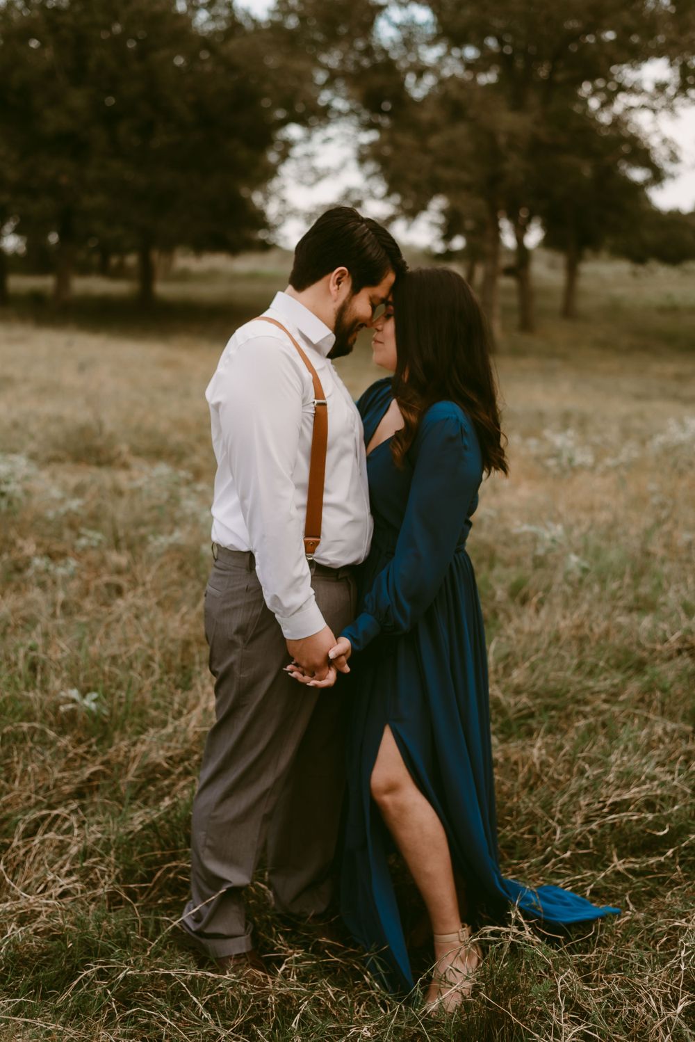 Couple shares romantic moment in field wearing navy dress and white shirt with brown suspenders.