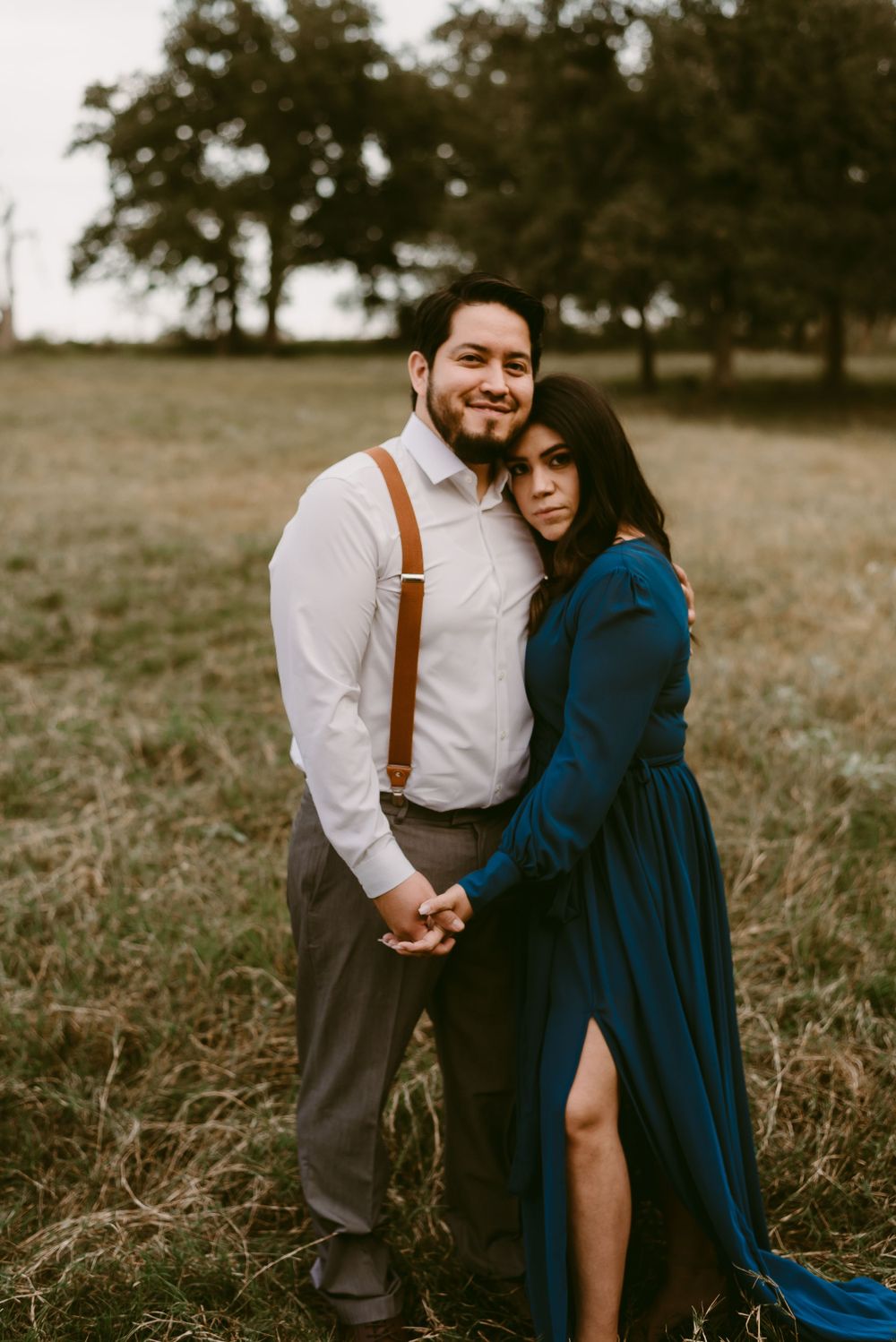 Intimate portrait of couple embracing in field wearing navy dress and white shirt with suspenders.