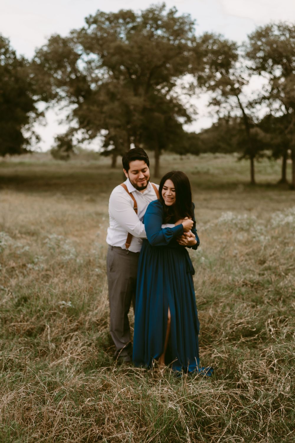 Happy couple laughing together in field wearing navy dress and white shirt with suspenders.