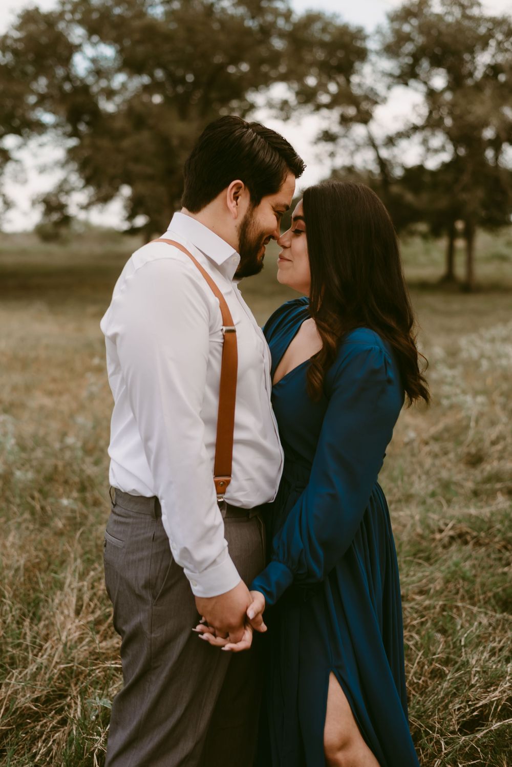 Intimate moment between couple in field wearing formal attire with navy dress and suspenders.