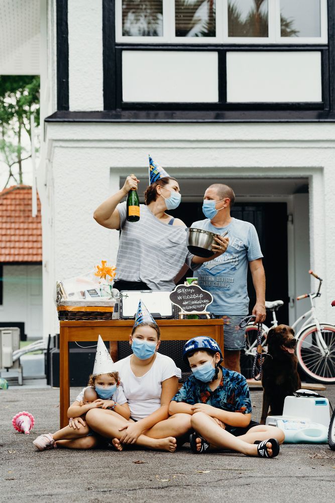A family of five pose outside their home during the pandemic, wearing masks and holding items important to them