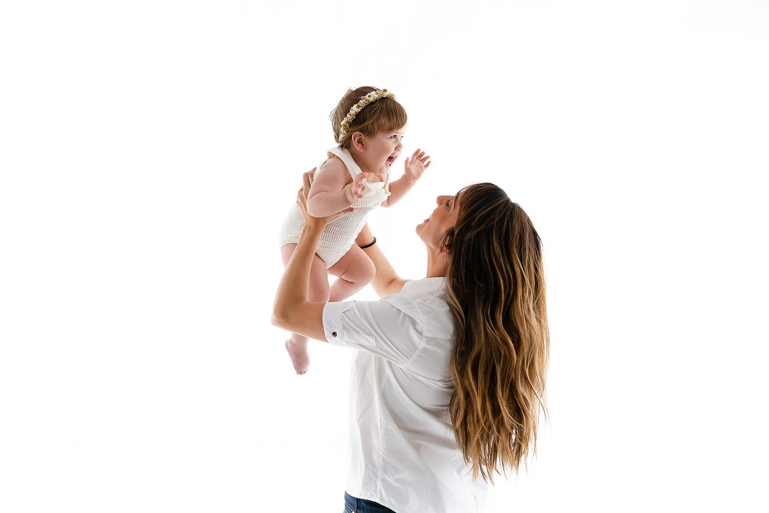 Sweet moment captured of parent lifting baby in white against bright background.