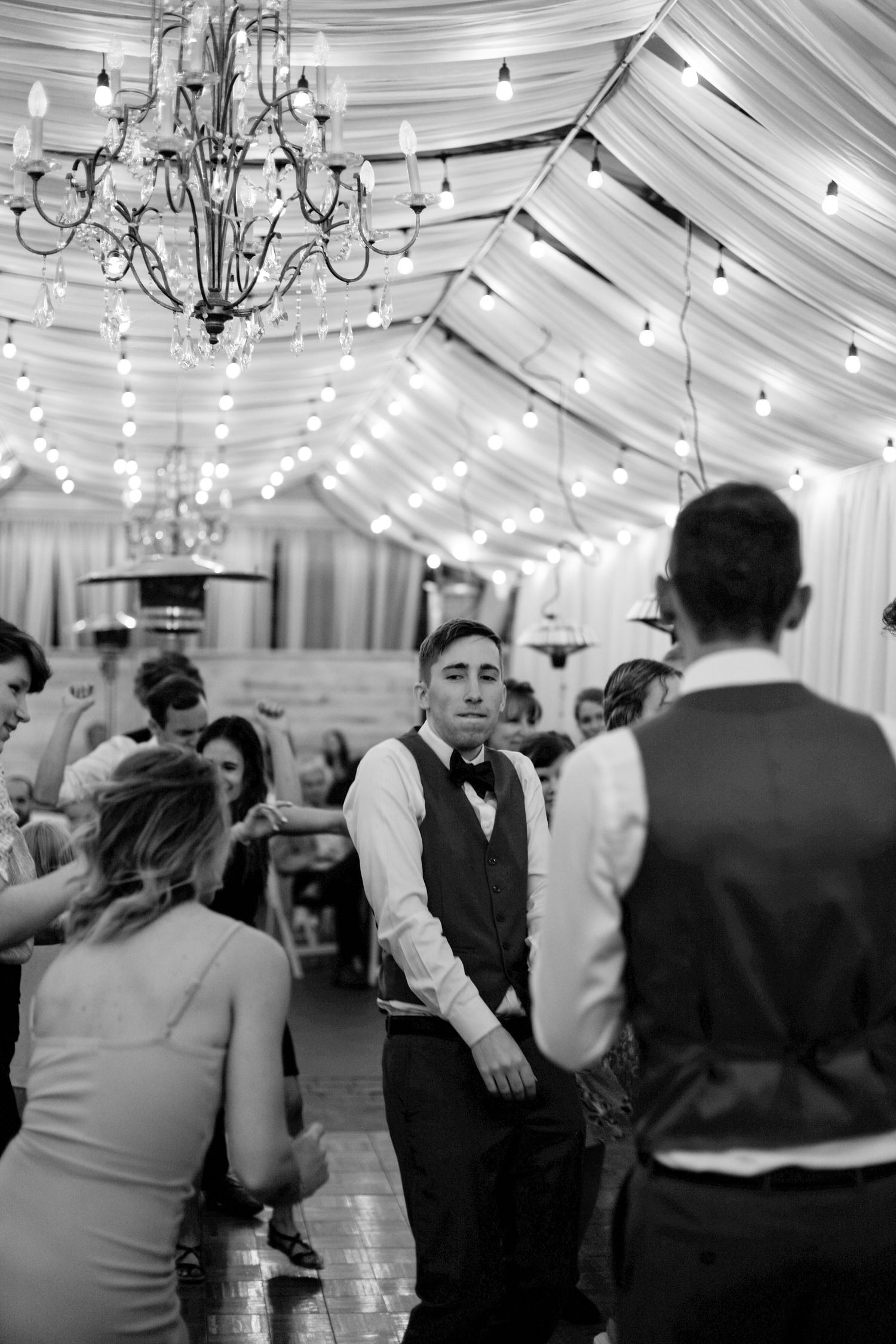 Wedding reception in an elegant tent with chandeliers and string lights creating a magical atmosphere.