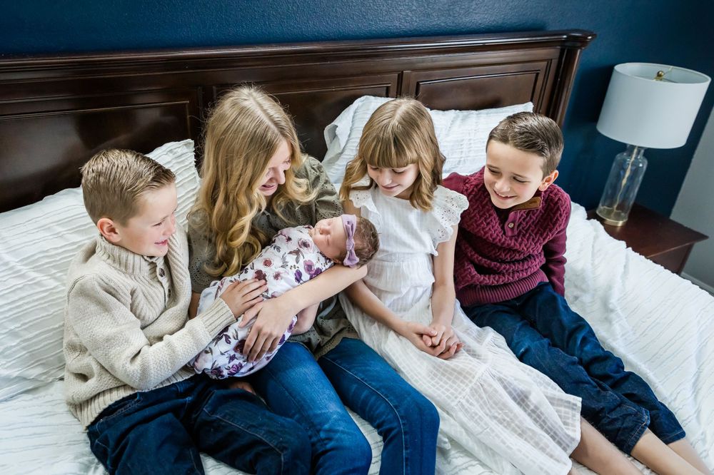 Children sitting together on a bed looking at a newborn baby.