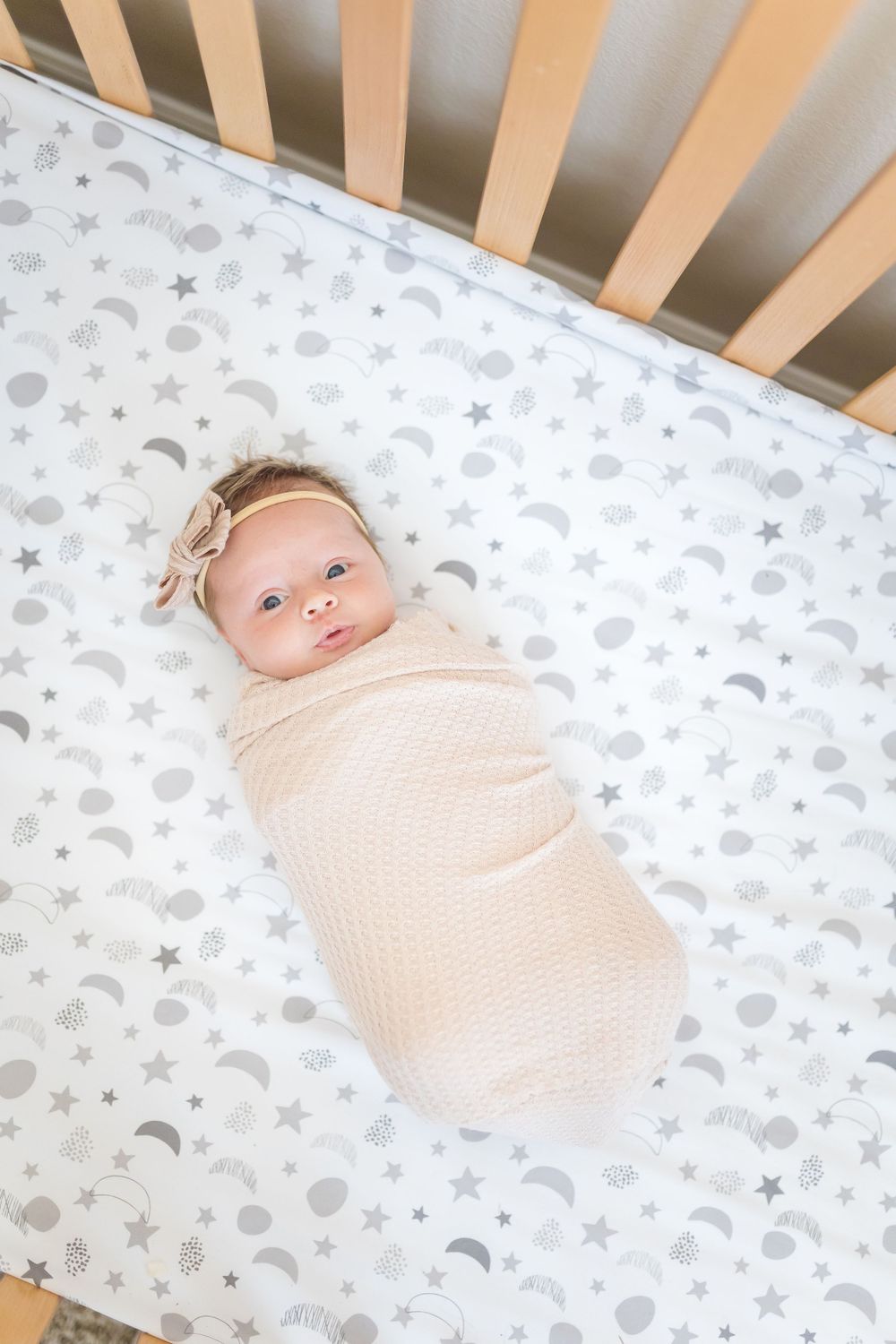 A baby rests in a crib with moon and star patterned bedding.