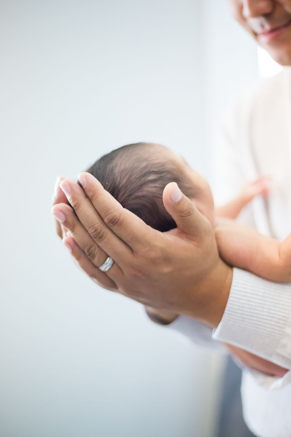 Gentle hands cradling a newborn baby's head against a light background.