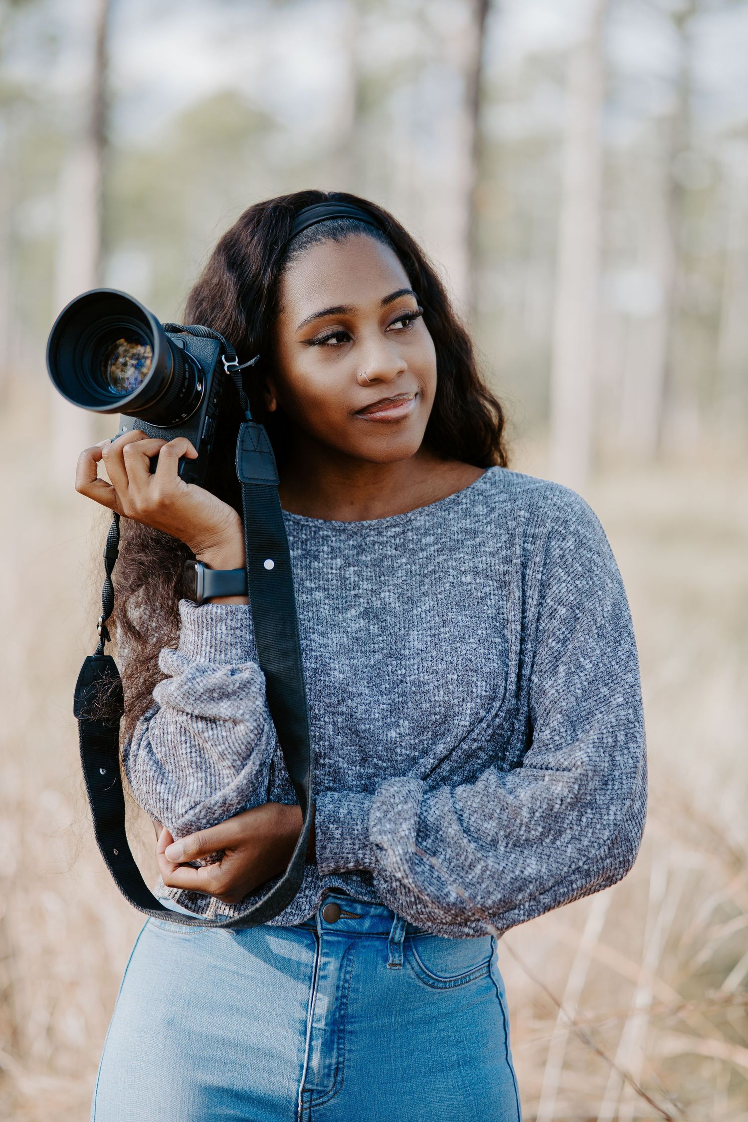 Young Black female photographer holding a DSLR camera in an outdoor autumn setting.
