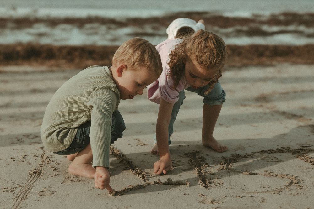 Children and adults bending down to examine something interesting in the sand at the beach.