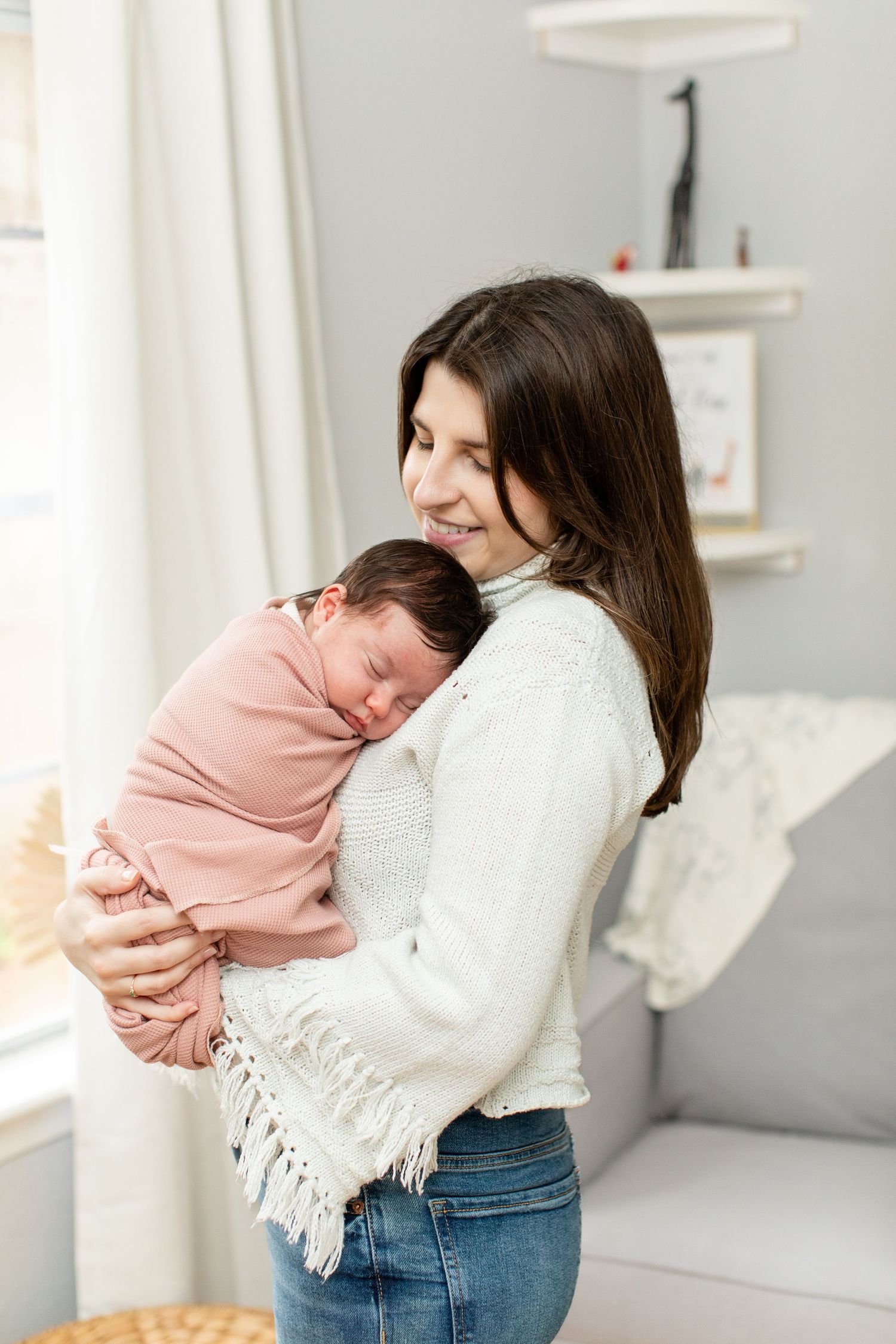 A woman in a white sweater holds and gazes lovingly at a baby wrapped in pink.
