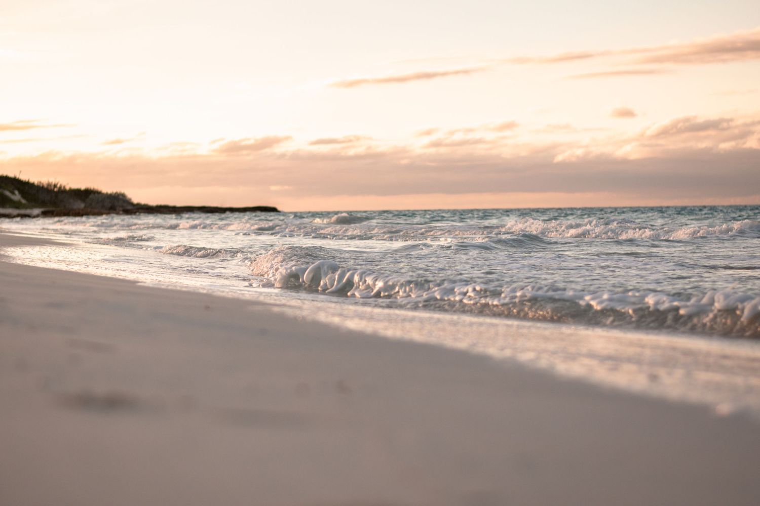 Gentle waves rolling onto a sandy beach during a peaceful sunset with pink and orange sky.