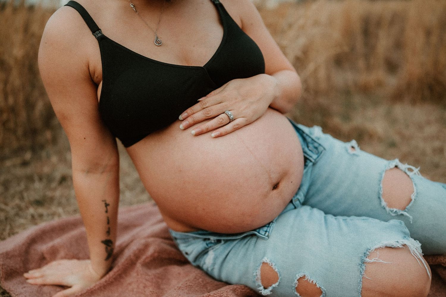 Close-up of a pregnant belly with ripped jeans on a blanket outdoors. rockford il