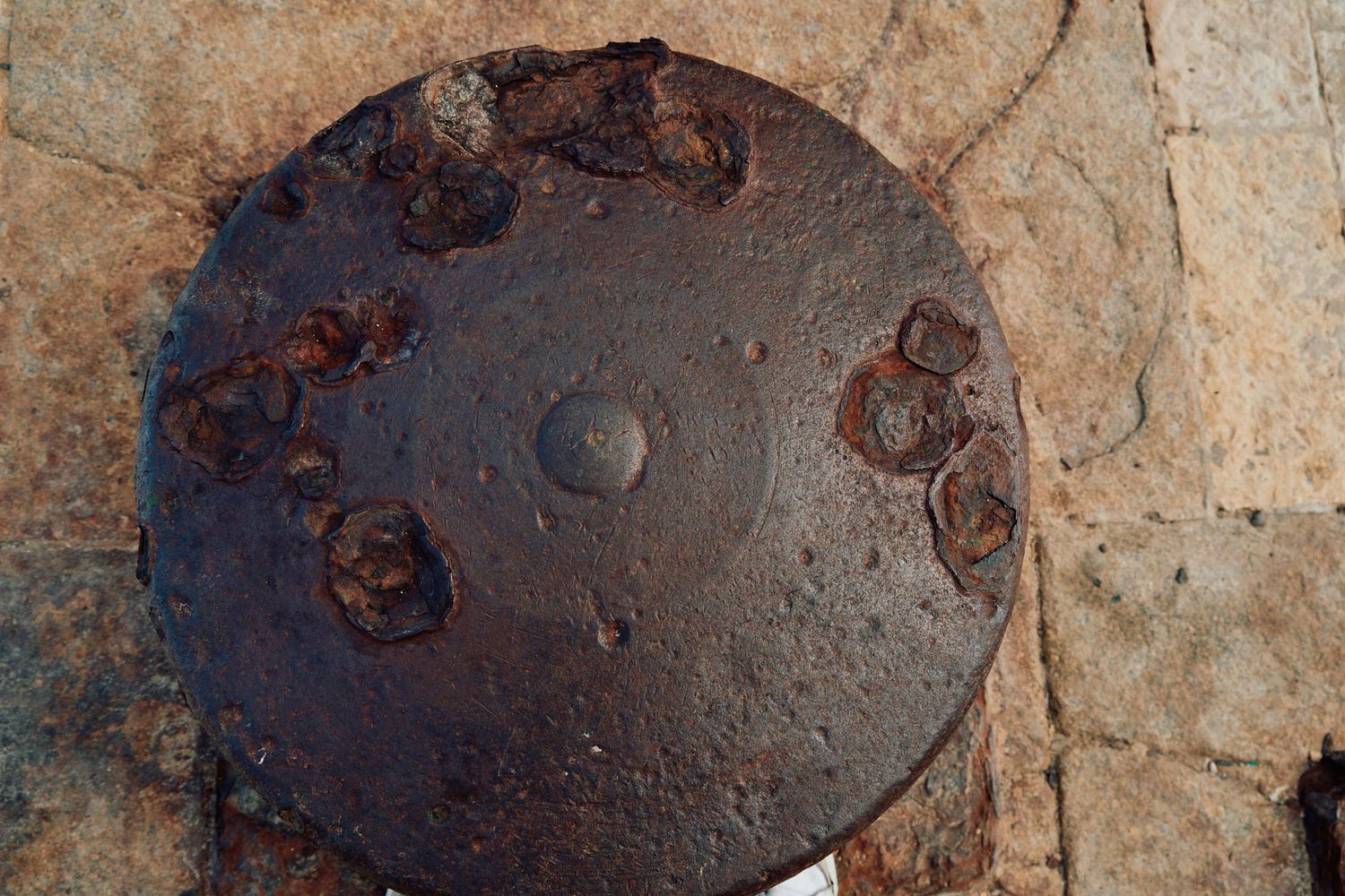 Close-up of weathered circular metal plate with rusted bolts on stone surface.