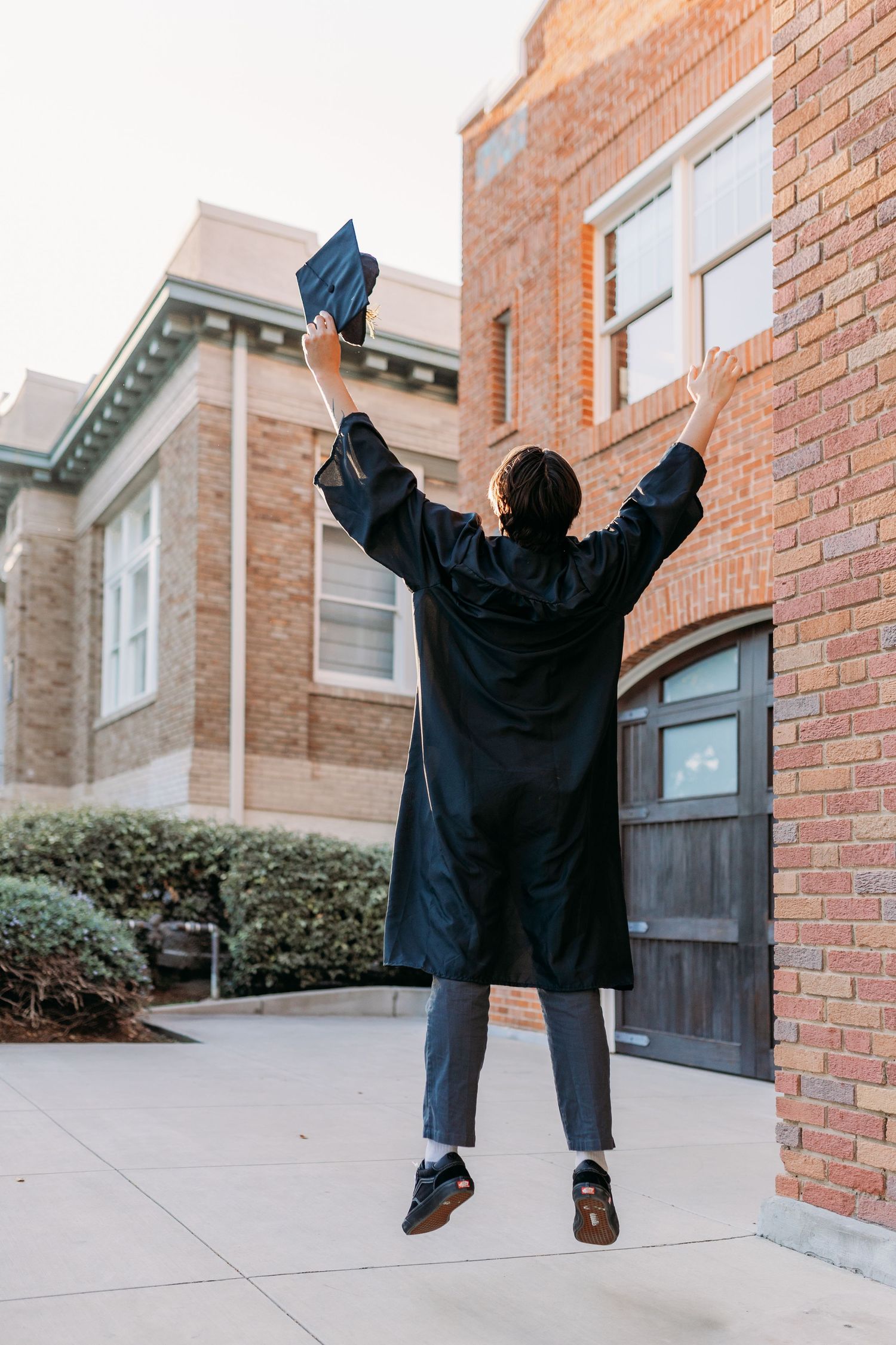 Recent graduate jumping in the air with his black cap and gown.