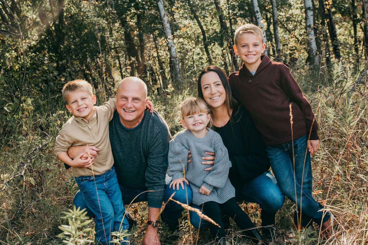 Five family members gather close together for a portrait in a woodland setting.