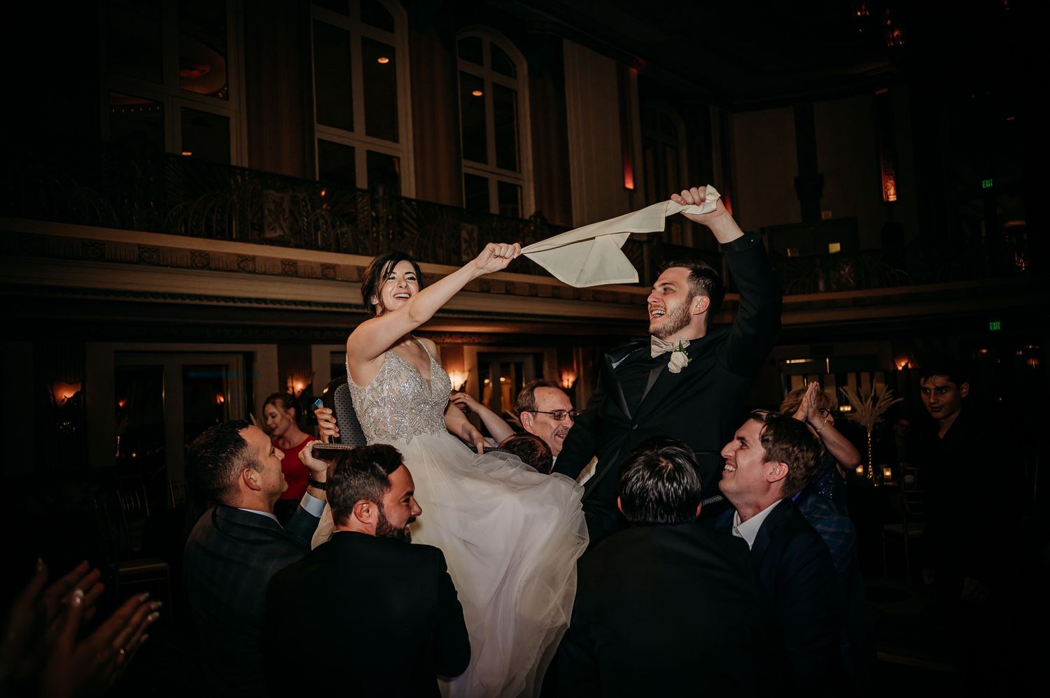 Bride and groom lifted by guests during lively Jewish wedding hora dance.