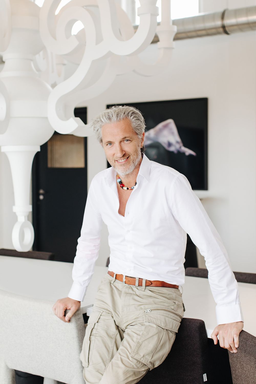 A person in white shirt and khaki pants sits casually in a modern office setting.