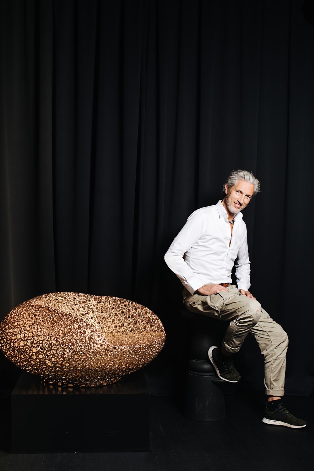 A person in white shirt sits on a black platform next to a decorative copper-colored sphere.