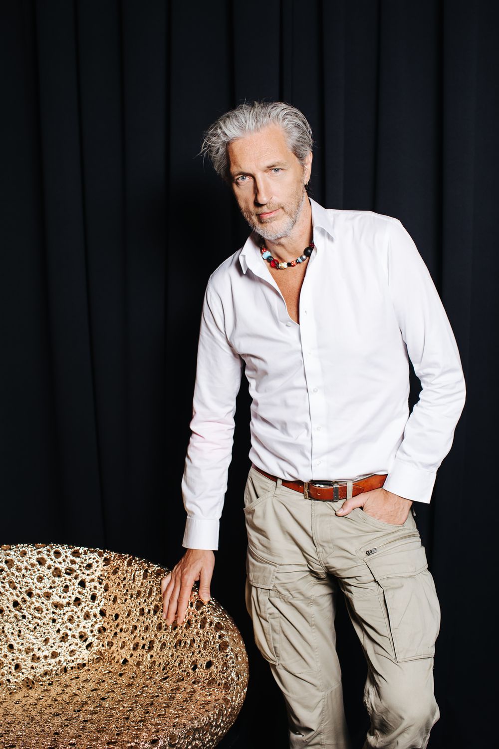 A person in crisp white shirt and cargo pants poses against a black backdrop.