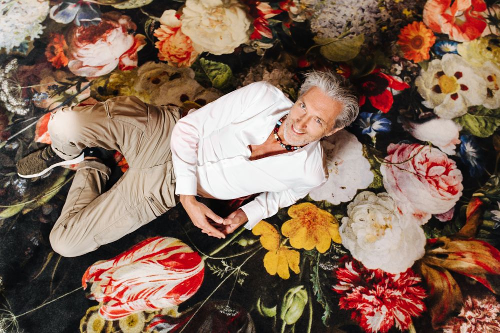 A person lies on a vibrant floral patterned surface wearing casual attire.