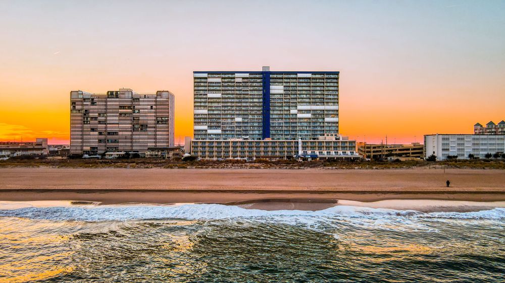 Aerial sunset view of beachfront high-rise hotels on sandy shore with orange sky reflecting on ocean waves.