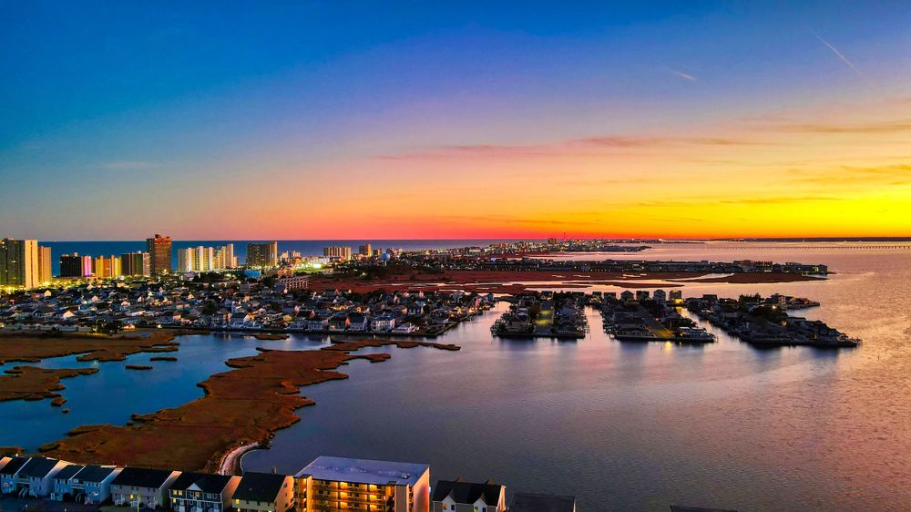 Aerial panoramic sunset view of coastal city marina with colorful orange and blue sky over waterways.