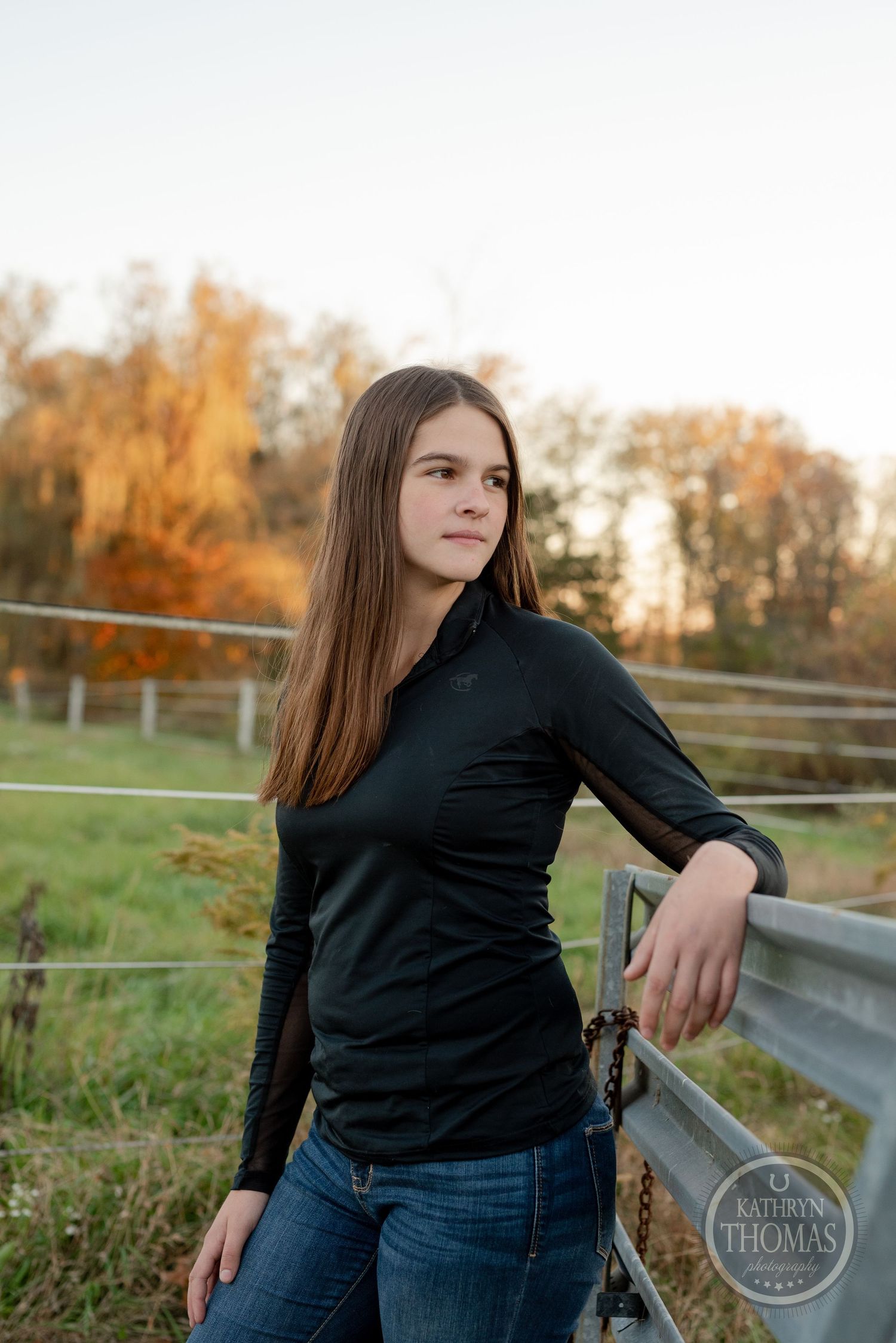 Casual portrait against rural fence with autumn trees in late afternoon light.