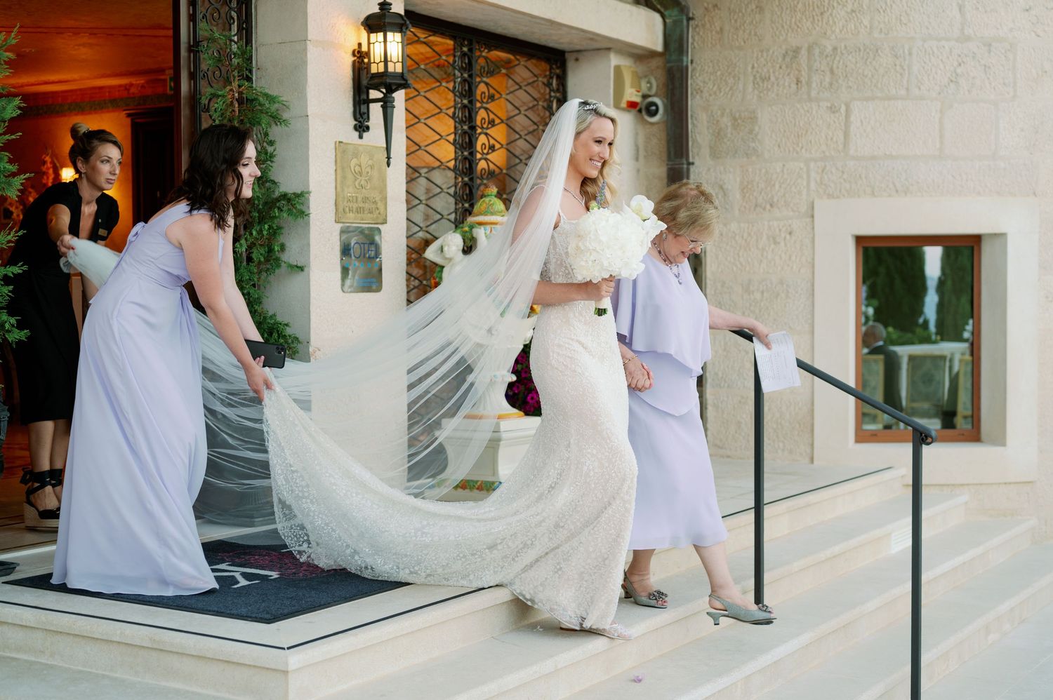 Wedding party walking up elegant stone steps with flowing white dress and veil.