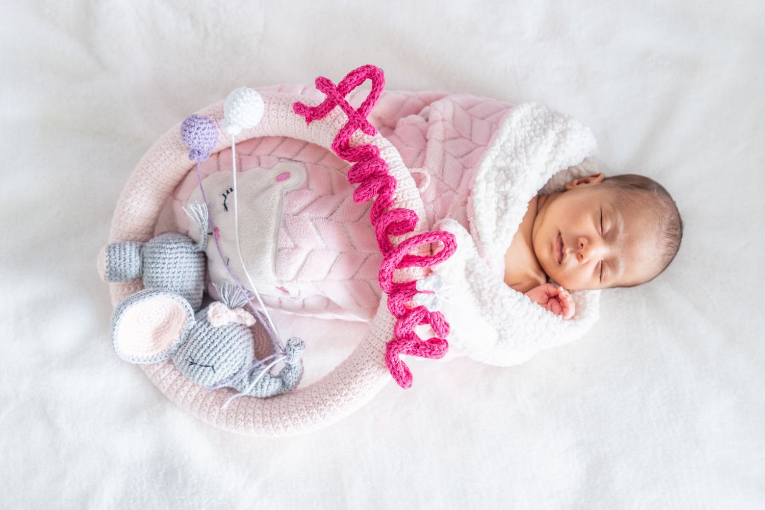 A sleeping newborn baby wearing pink and white clothing lies on a soft white blanket.