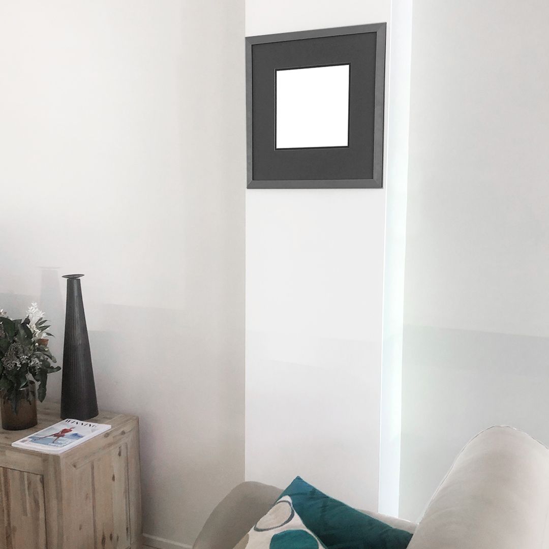 Minimalist interior design featuring a single black square frame on white wall above wooden furniture.