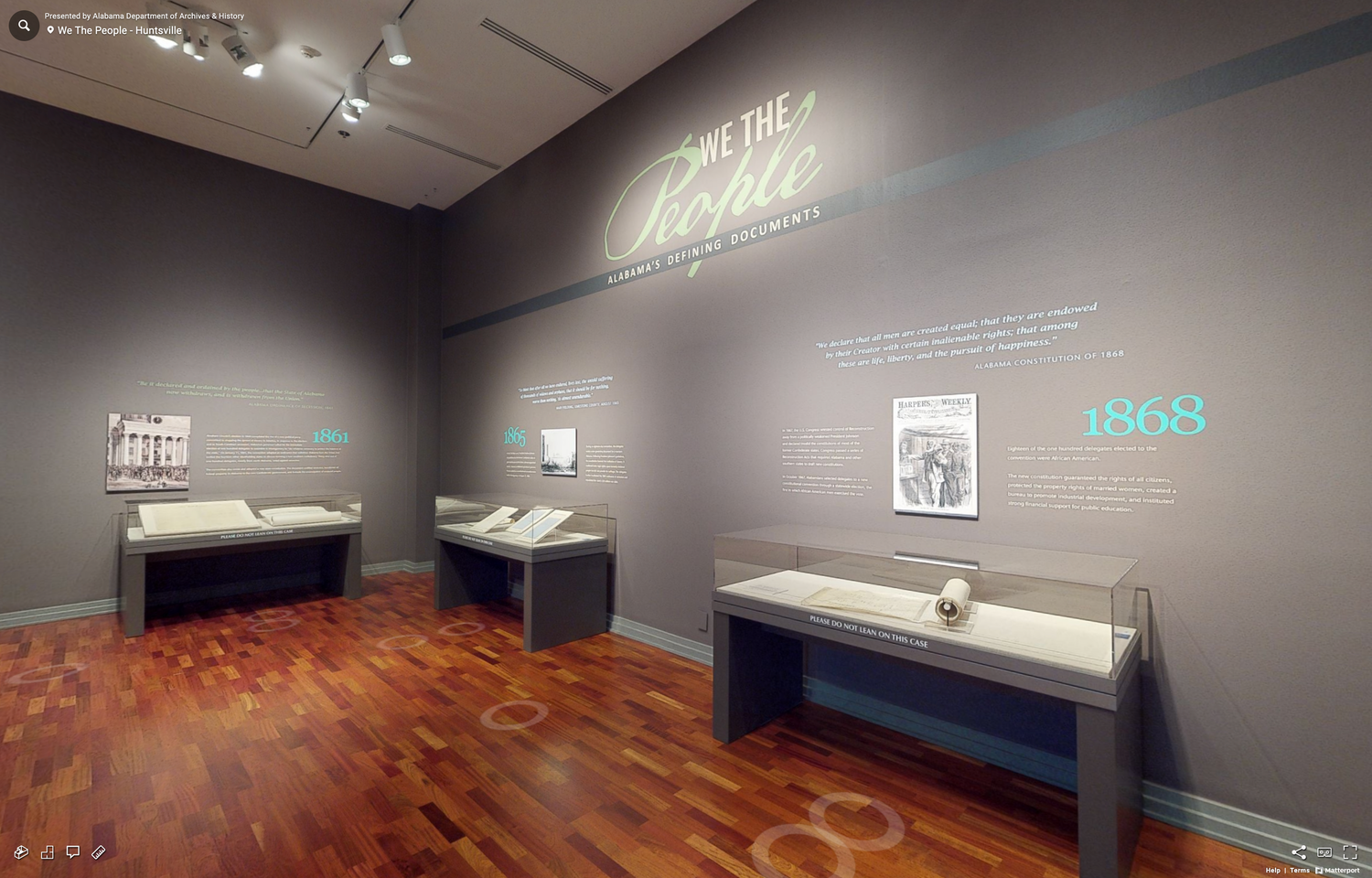 Museum exhibition space with display cases and illuminated text on dark walls.