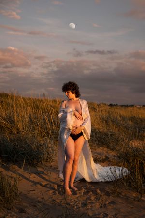 Artistic beach portrait with figure in white shirt against sunset sky with moon visible.