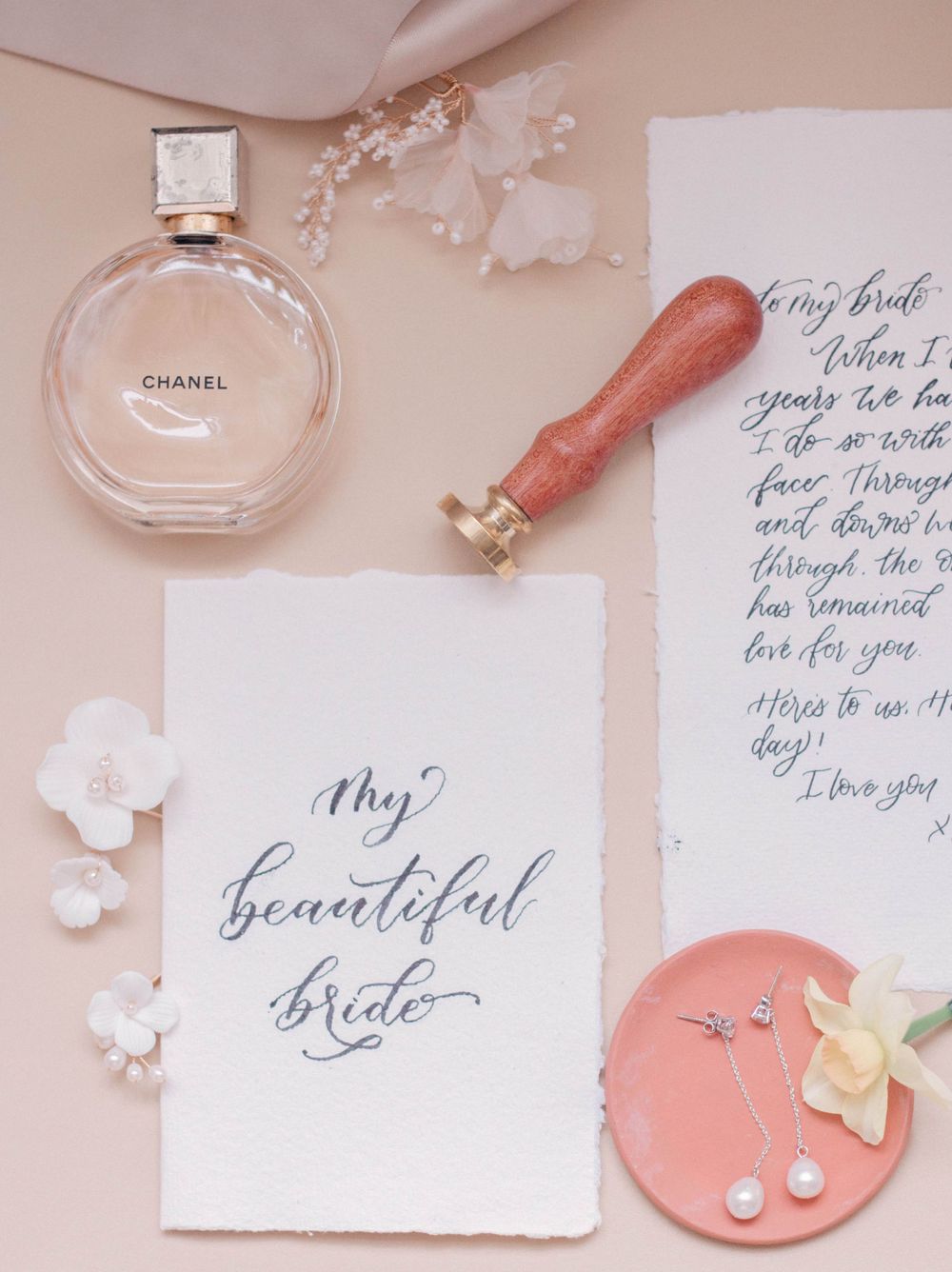 Wedding details flatlay with calligraphy notes, perfume bottle, and coral accents.