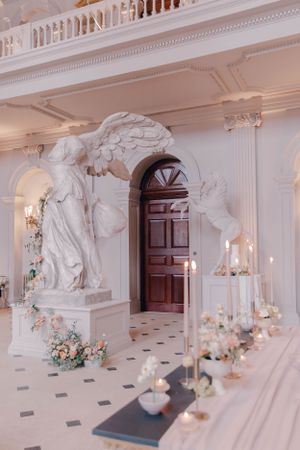 Luxurious white marble hallway with classical statues and floral arrangements.