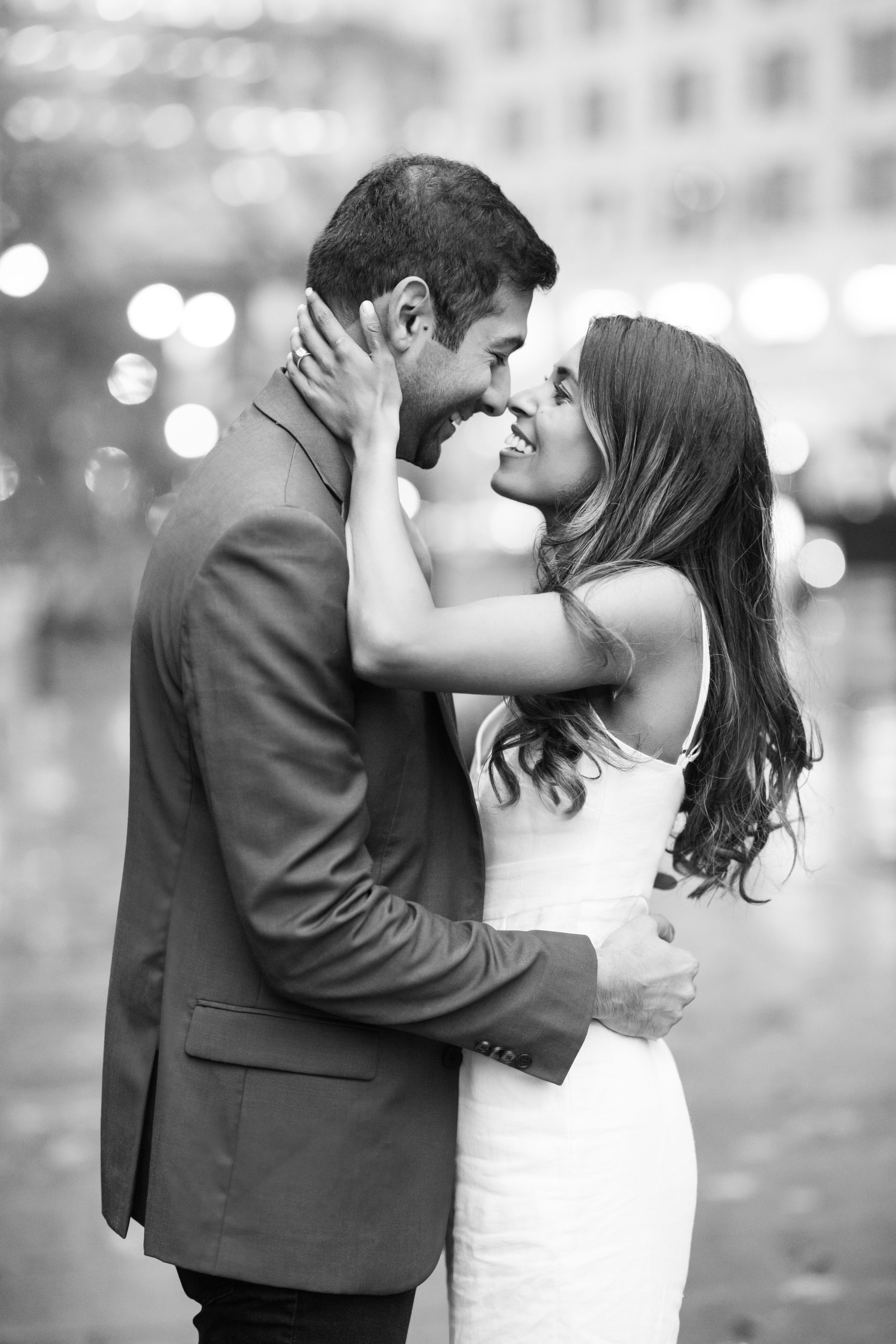 Black and white romantic couple almost kissing with bokeh city lights in background.
