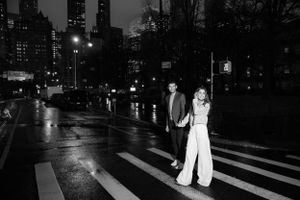 Black and white photo of couple holding hands crossing wet street at night in NYC.