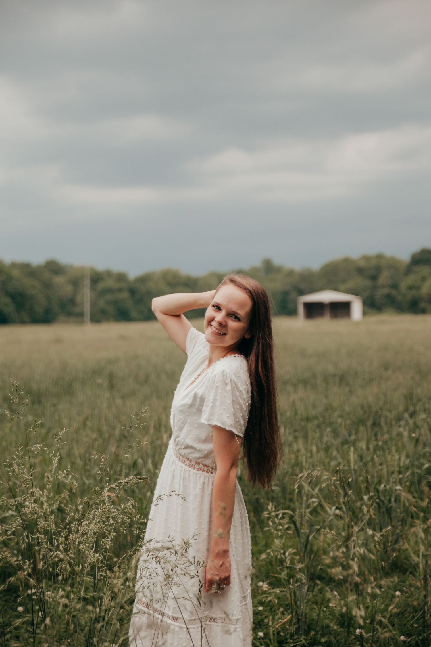 Woman in white lace dress poses gracefully in summer meadow.