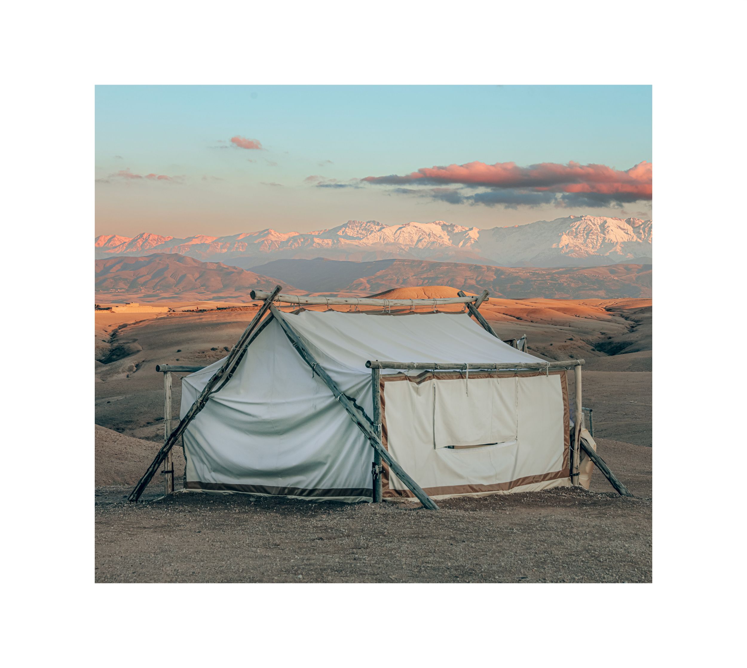 Canvas tent setup in desert landscape with mountains in background at sunset.