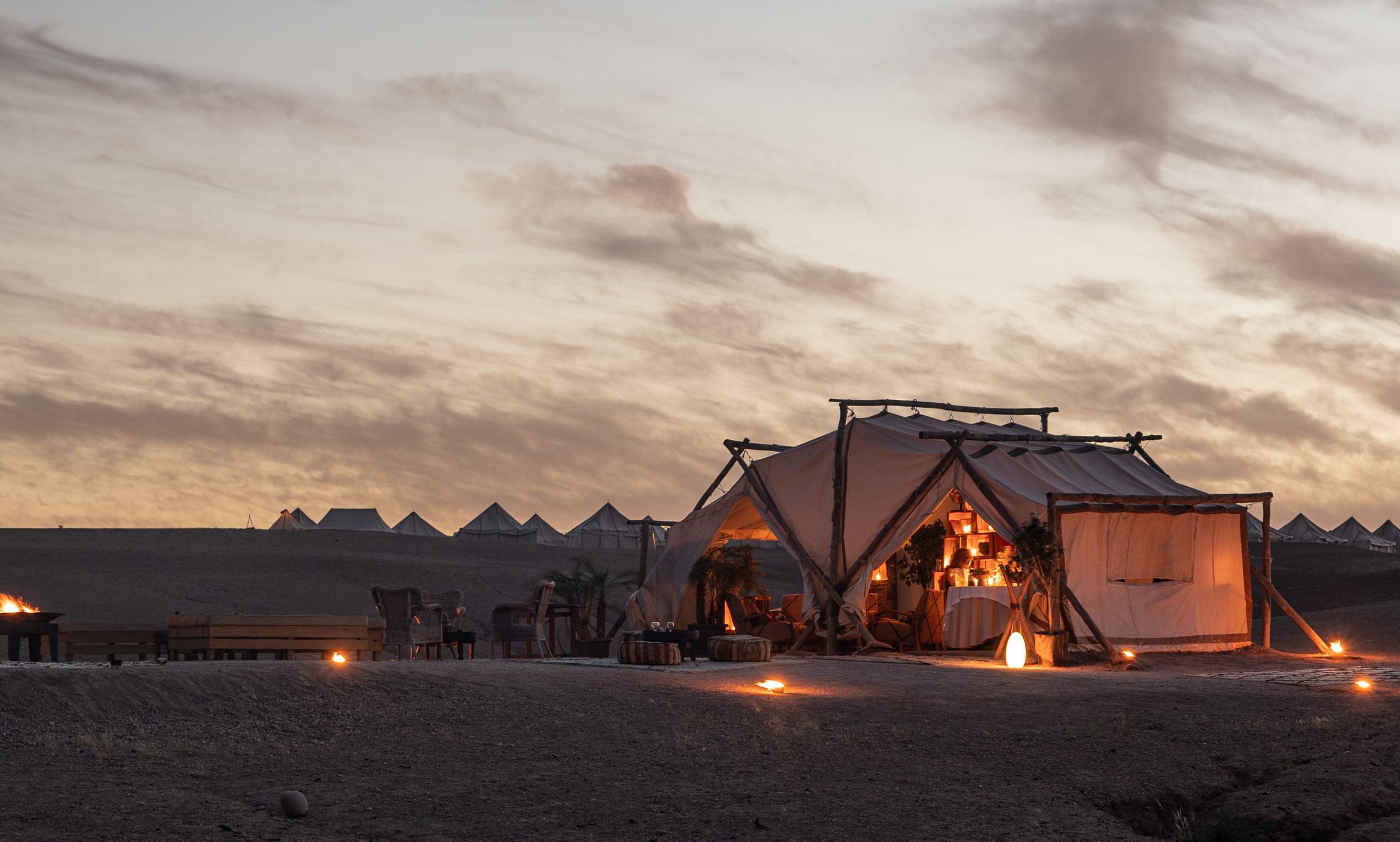 Glowing tents illuminated at dusk in desert setting with warm lighting.