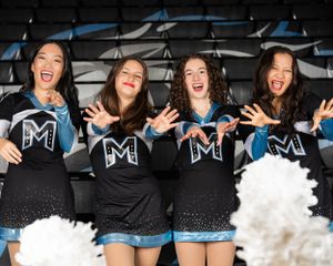 High school dance team in black and blue uniforms laugh and pose together in stadium bleachers.