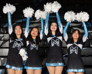High School Dance Team dancers in black uniforms with M logos wave white pom poms during a spirited stadium performance.