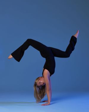 Athletic high school dancer in black workout attire executes a graceful handstand pose against a blue backdrop.