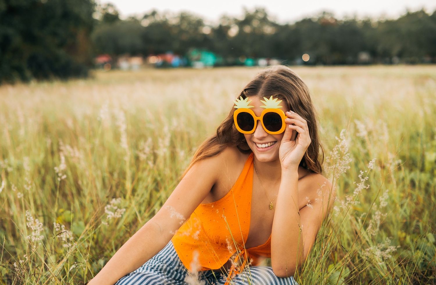 Person wearing orange top and sunglasses poses playfully in summer field.