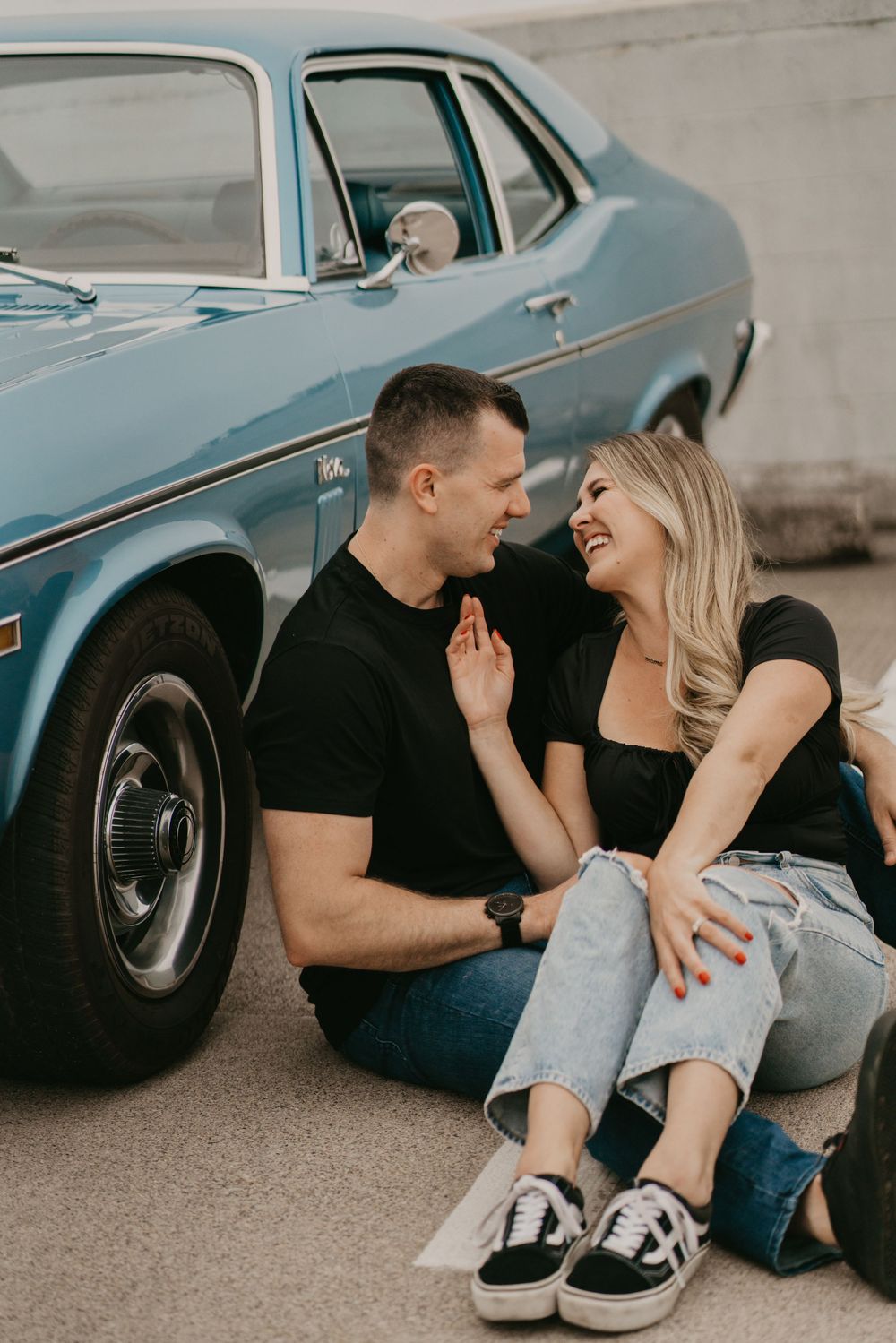 Couple sitting intimately by classic blue car sharing romantic moment.
