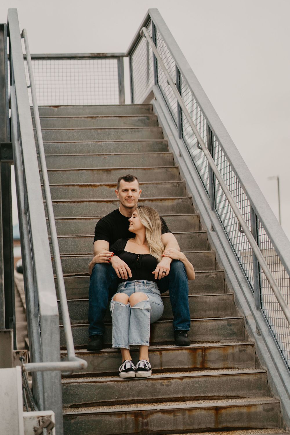 Couple sitting close together on industrial metal stairs during urban photoshoot.