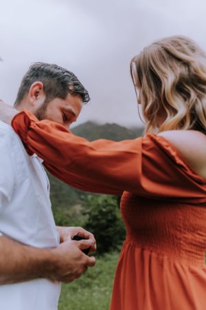 Couple in white shirt and rust dress sharing tender moment in mountain setting.