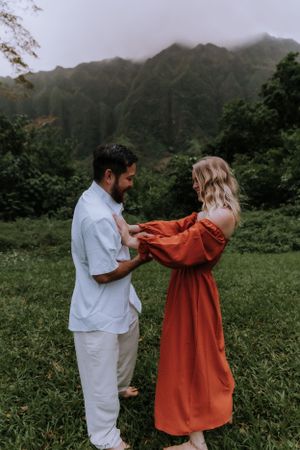 Two people share a lighthearted moment in casual attire with lush mountains in the background.