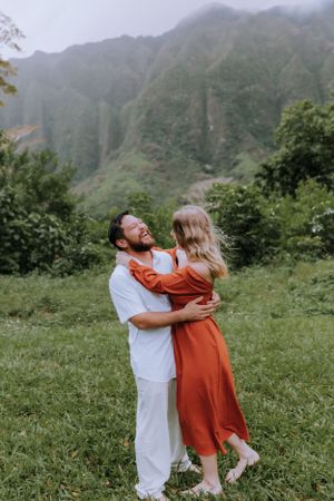 Joyful couple dancing in white and rust attire with mountains in background.